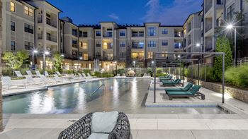 An apartment swimming pool with lounge chairs at night
